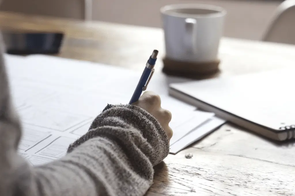 person writing notes near a white mug - featured image