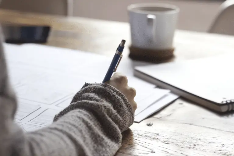 person writing notes near a white mug - featured image